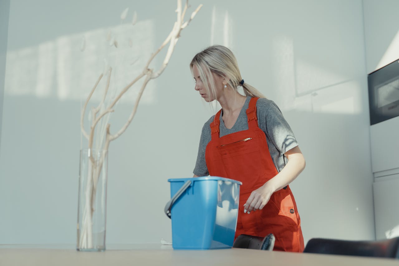 brand-02 A woman in a red uniform cleans indoors with a blue bucket, ensuring a spotless environment.