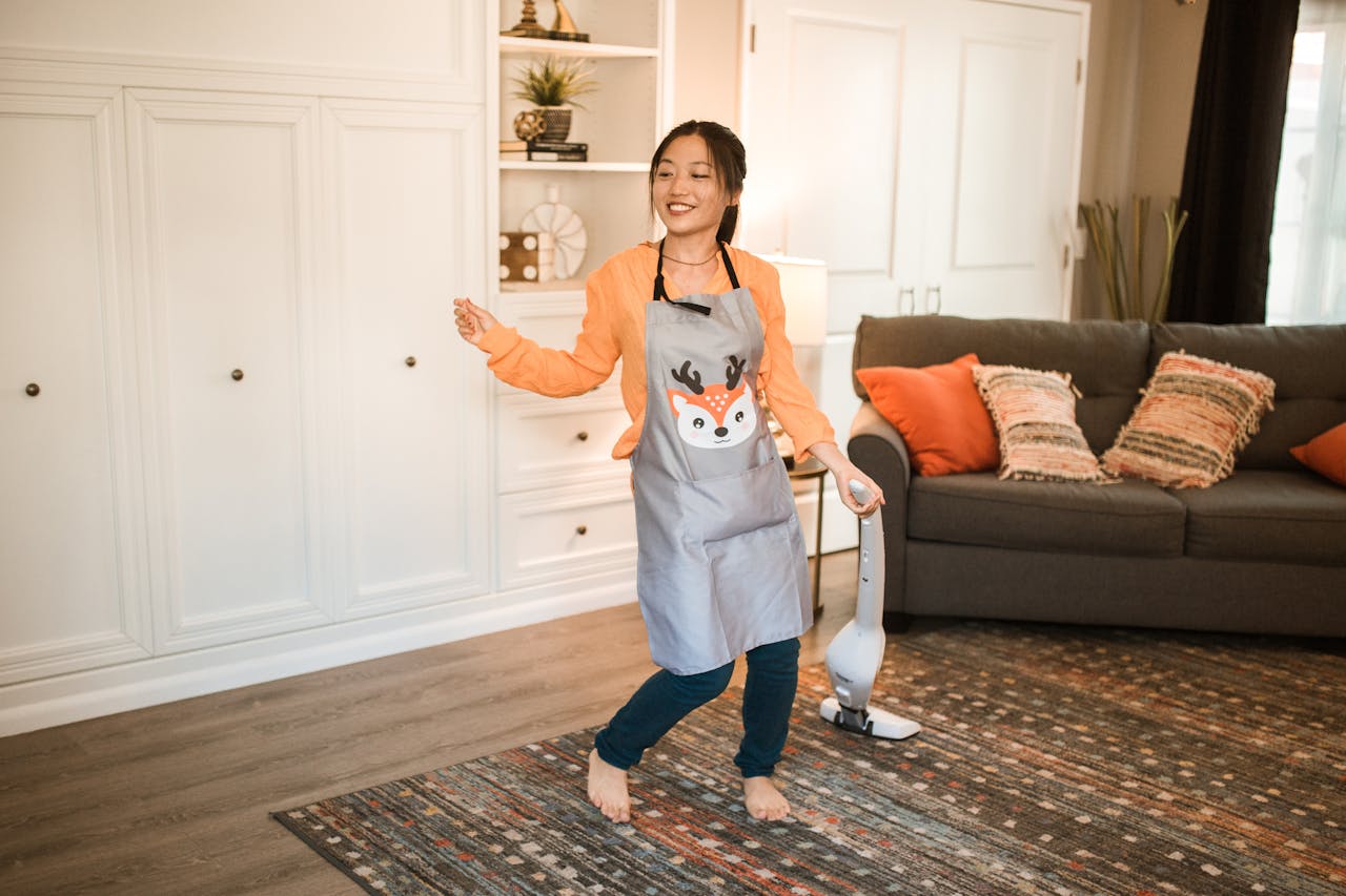 creative-01 Asian woman happily cleaning her living room with a vacuum. Bright, cheerful indoor setting.